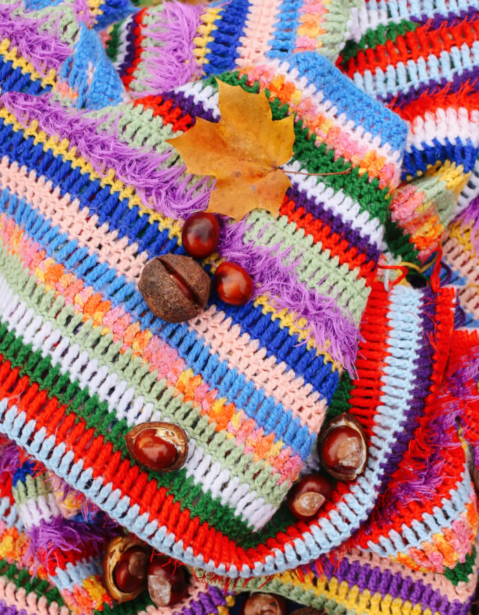 Autumn background. Horse chestnuts and maple leaf on crocheted bright warm striped plaid.