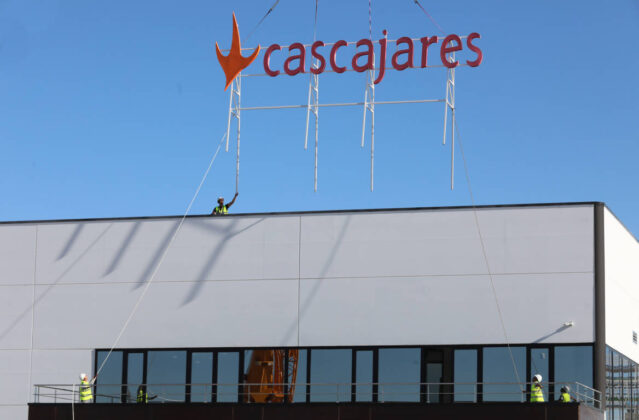 Responsables y trabajadores de Cascajares y de las empresas constructoras junto al cartel de Cascajares que sobrevivi&oacute; al incendio y que se ha vuelto a recolocar en las nuevas instalaciones. / Br&aacute;gimo (ICAL)